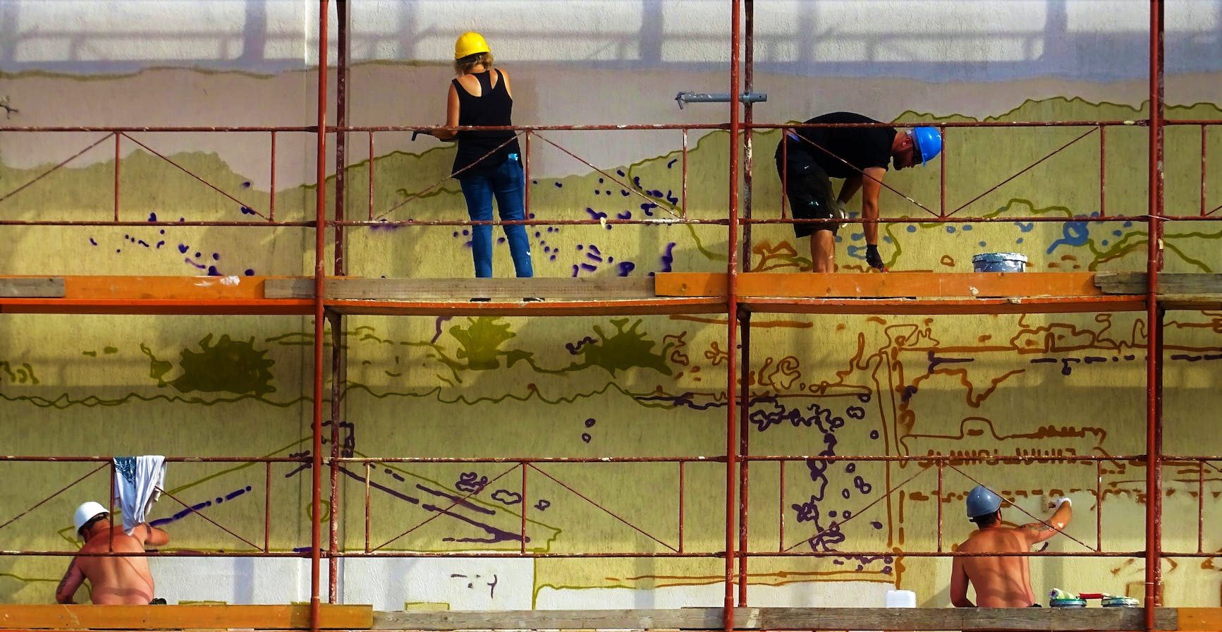 four people painting wall on scaffolding